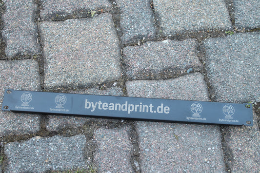 Graue Blindabdeckung mit gravierten Rundmotiven und byteandprint.de-Aufdruck auf Pflaster