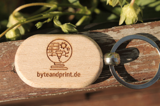 Runder Holz-Schlüsselanhänger mit Lasergravur und Metall-Schlüsselring, Text „byteandprint.de“.