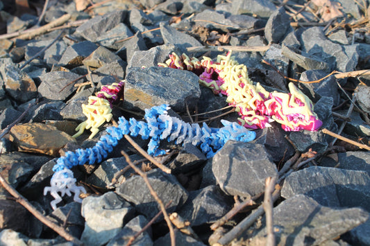 3D-Element-Drache mit blauem und mehrfarbigem Kamm auf Steinen