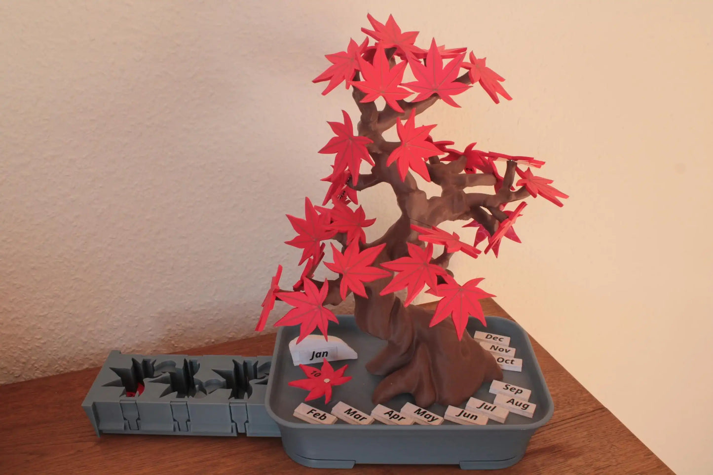 3D printed tree calendar with red paper leaves and labeled months on a wooden table