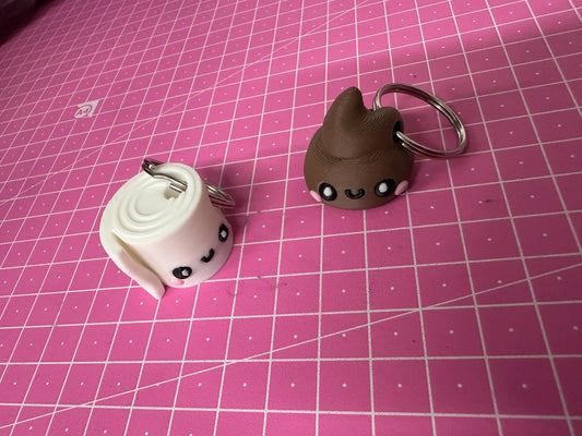 Cute kawaii toilet paper and poop keychains with smiling faces on a pink grid mat