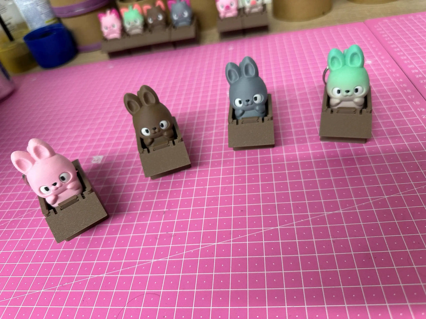 Cute bunny figurines in brown boxes on a pink crafting mat, collectible toy display