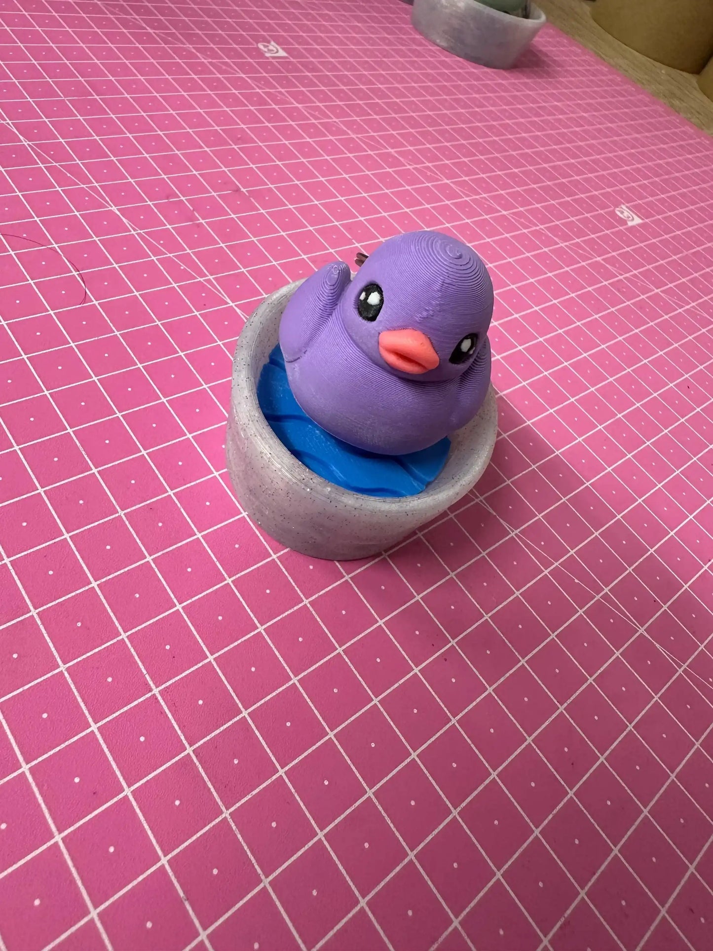 Purple 3D printed bird figurine in gray and blue bowl on pink grid cutting mat