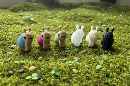 Strick-Schneckenfigur auf Rasen: mehrere beige, eine weiße und eine schwarze Schnecke